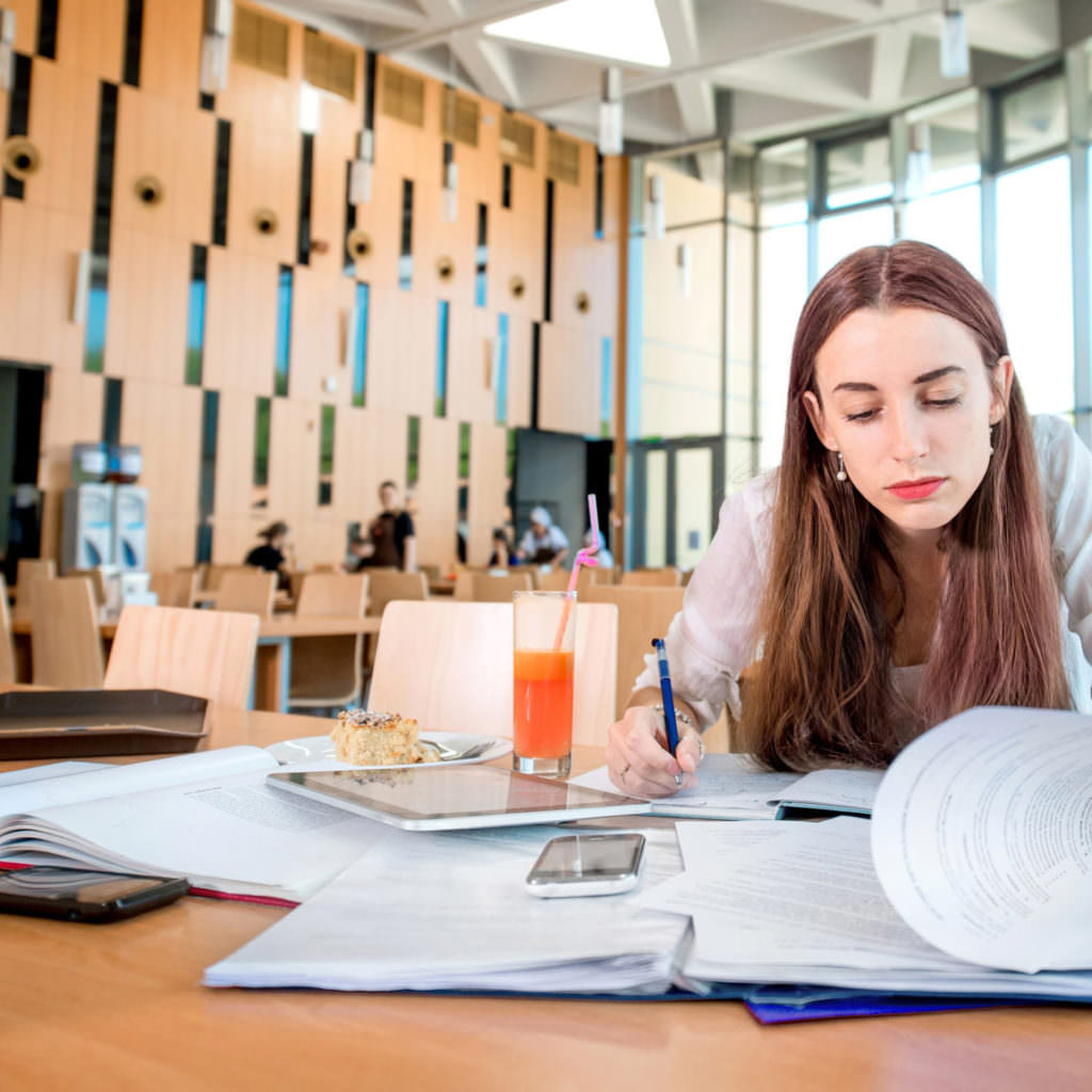 Girl studying in the University canteen with  cake