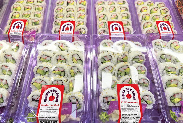 Rows of packaged grab-and-go sushi containers featuring custom-branded retail prepared foods labels lined up in a grocery store display case